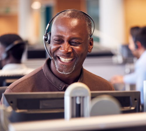 A man with a headset smiling at his computer screen.