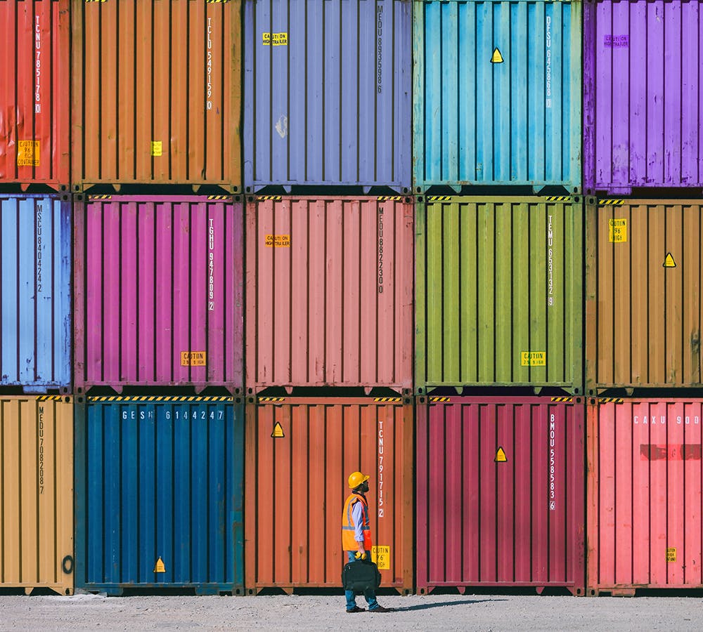 A worker standing in front of a stack of coloured shipping containers | fx international payments
